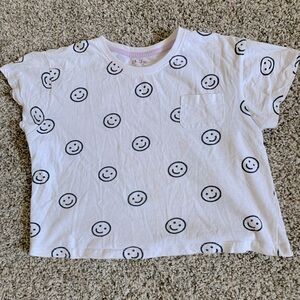 White shirt, black smiley faces, a pocket. Small grey stain (pictured).